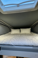 Cozy pop-top bed in an RV rental, featuring white bedding and a skylight for natural light in the sleeping area.