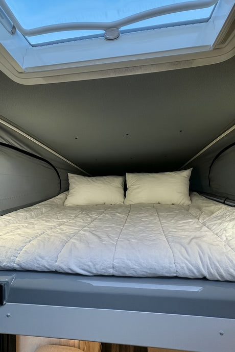 Cozy pop-top bed in an RV rental, featuring white bedding and a skylight for natural light in the sleeping area.