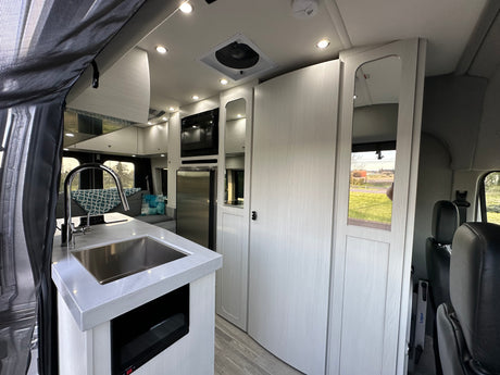 Modern RV rental interior: kitchen with sink, microwave, fridge, sleek white cabinets, and LED lighting. Bright and functional space.