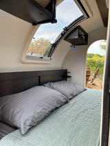 RV rental interior: cozy bedroom with large window, offering an inviting view of nature and outdoor chairs.