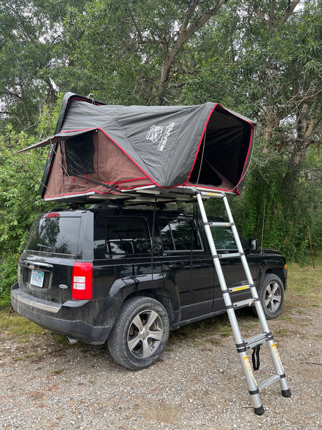  parked on grass. Perfect for an RV rental camping adventure!|A black Jeep Patriot with an iKamper rooftop tent set up for camping