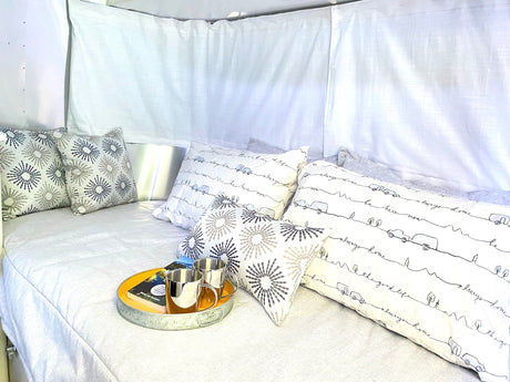 Relax in this cozy RV rental bed/lounge area. Features decorative pillows, a book, and mugs on a tray for comfort.