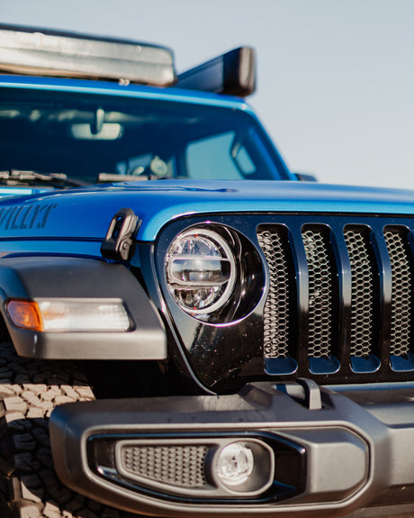 Close-up of a blue Jeep Wrangler Willys' front, showing headlight, grill, and roof storage. Explore with an rv rental.