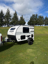 White Sunray Sport travel trailer for rv rental, parked on grass. Truck, trees, and cloudy sky in background.