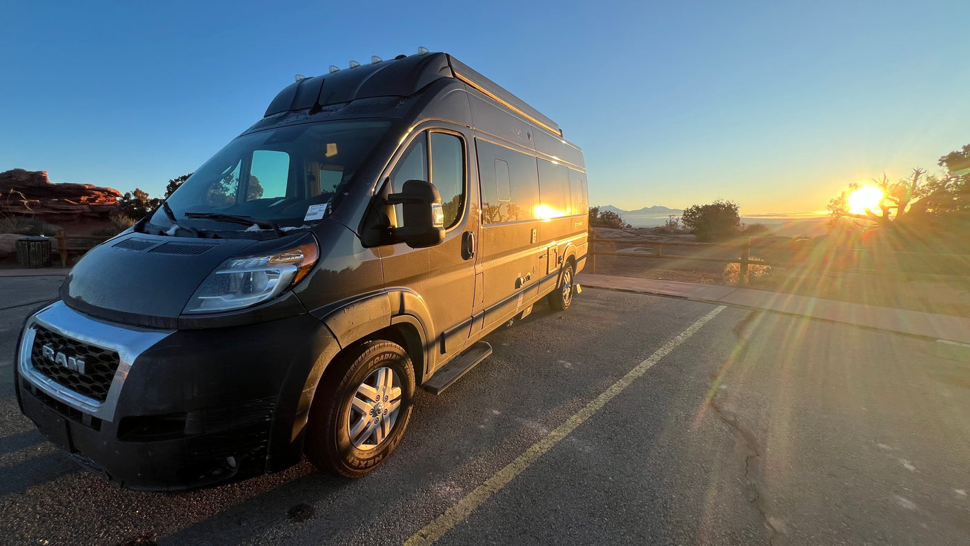 Golden sunrise illuminates this RV rental camper van, parked at a scenic overlook with distant mountains, perfect for a road trip.