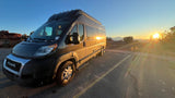 Golden sunrise illuminates this RV rental camper van, parked at a scenic overlook with distant mountains, perfect for a road trip.