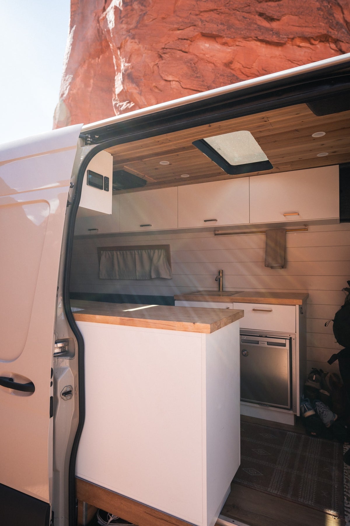 Stylish RV rental interior: custom kitchen with wood counters, sink, fridge, and controls in a sunlit camper van. — photo 2