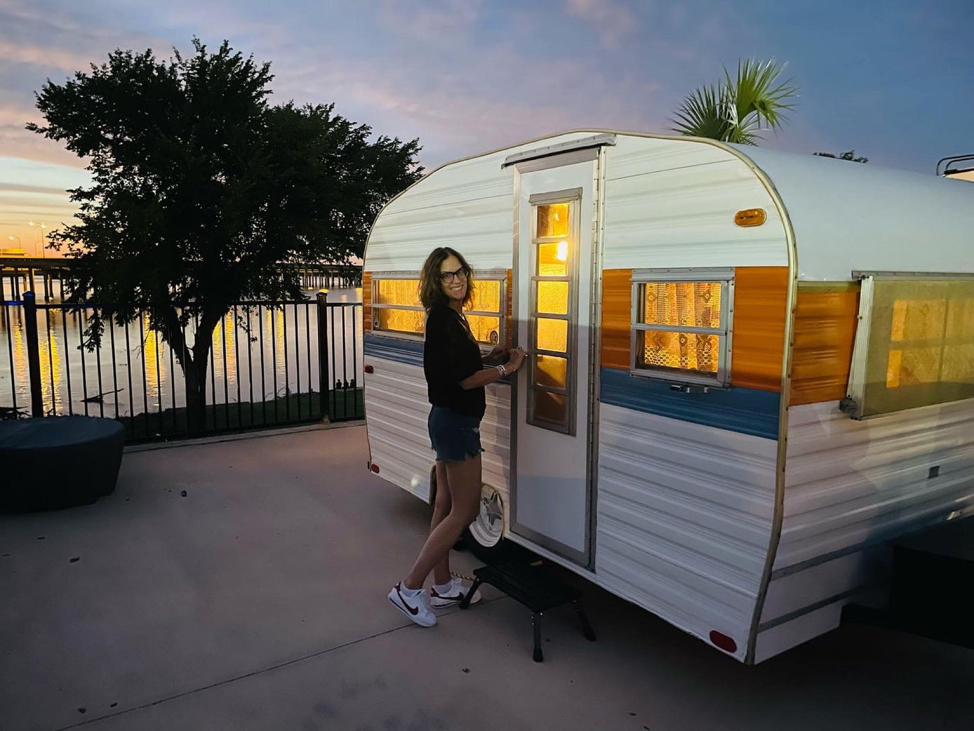 Experience the joy of camping! A happy woman with her colorful RV rental at sunset by the lake.