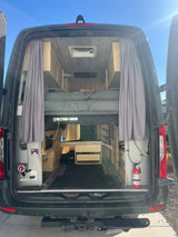 Inside a well-equipped camper van conversion, an RV rental option. Features a raised bed, storage, and practical utilities.