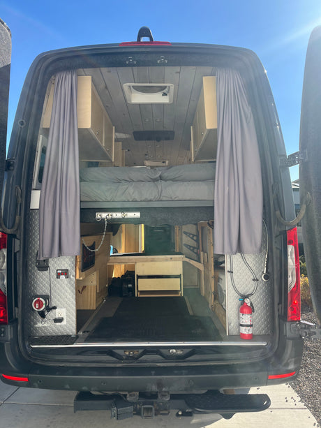 Inside a well-equipped camper van conversion, an RV rental option. Features a raised bed, storage, and practical utilities.