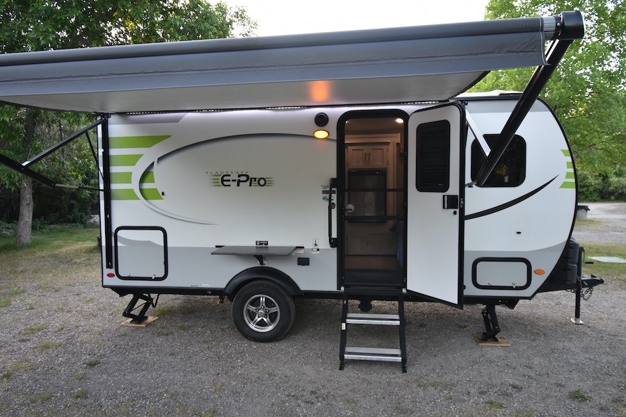A white & green Flagstaff E-Pro rv rental with an extended awning, open door, and stairs, parked on a gravel campsite. — photo 7