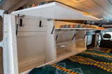 Inside a compact RV rental: Lift-up storage with gas struts, shelving, and a cozy bed, optimizing space for adventures.