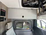 RV rental interior: A Winnebago camper van with light gray overhead storage, control panel, and a window shade featuring palm trees.