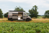 Custom grey camper van RV rental parked in fields, showing its open side door kitchen. Perfect for outdoor travel.