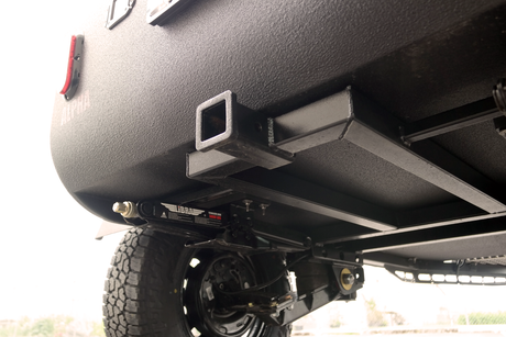 Rear underside of an RV rental: robust hitch receiver, stabilizer jack, and textured body for durability.