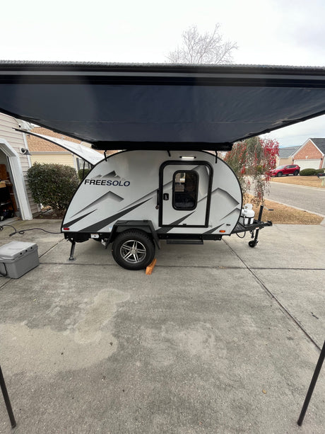 FREESOLO teardrop RV rental, a compact travel trailer with its awning extended, parked on a driveway.