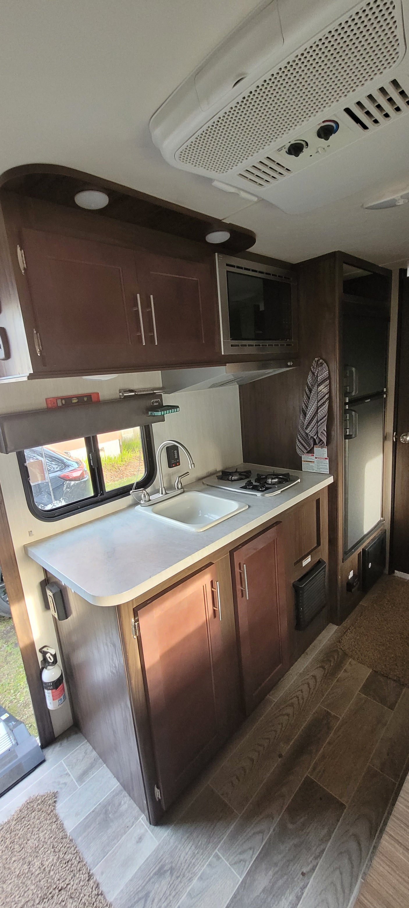 Explore this rv rental's compact kitchen with a sink, stove, microwave, dark cabinets, and an overhead AC unit.