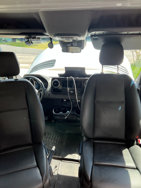RV rental front cabin: black leather seats, dashboard controls, and open hood visible through the windshield.