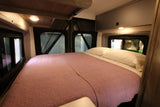 Cozy RV rental bedroom with a large bed, pink quilt, white pillows, and soft lighting, ideal for comfortable travel.