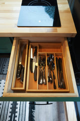 Top-down view of an RV rental kitchen: wood countertop, induction cooktop, and neatly organized cutlery drawer.