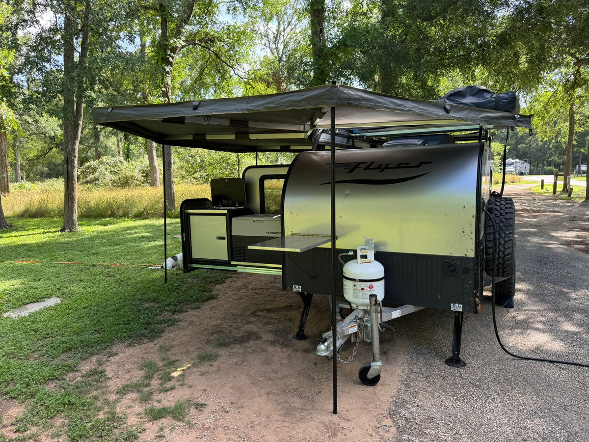 An RV rental, an off-road camper with an extended awning and outdoor kitchen, is set up at a leafy campsite. — photo 2