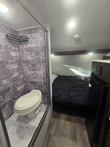 Compact rv rental interior showing a shower/toilet combo, bed, and small fridge, offering a complete living space for travel.