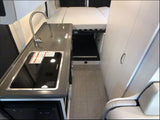 RV rental's compact interior features a kitchenette (sink, stove), bed with under-storage, and white cabinets.