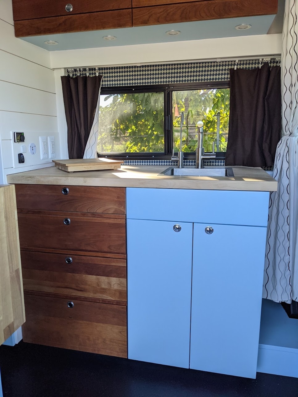 Custom RV rental kitchen featuring light wood counters, blue cabinets, sink, and a scenic window view. — photo 3