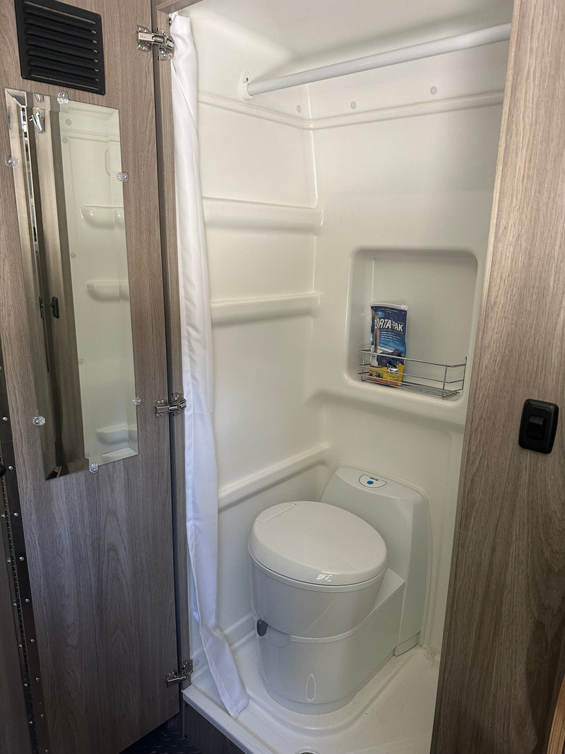 RV rental wet bath featuring a compact toilet, integrated shower, and storage rack for essentials. — photo 12