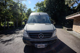 Grey Mercedes Sprinter van, an RV rental, parked on an asphalt drive with tropical trees and a building.