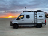 Experience van life freedom! A silver RV rental, a Winnebago Revel 4x4, parked on a beach at a vibrant sunset.