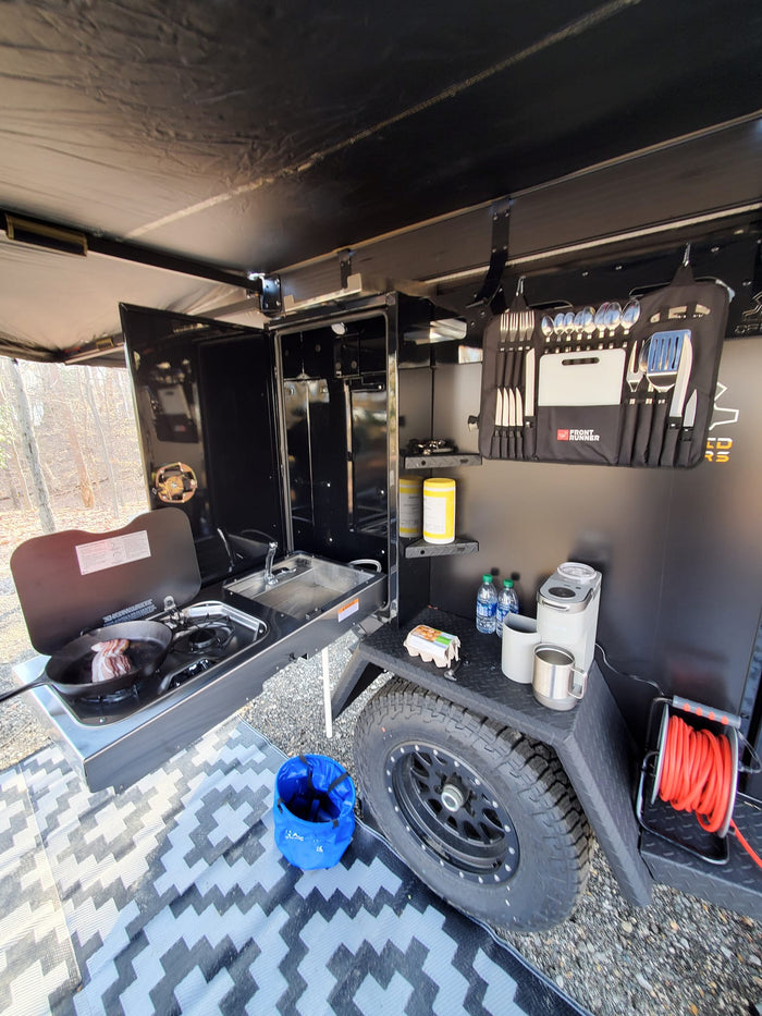 RV rental outdoor kitchen. Cooking bacon, sink, coffee maker, and organized utensils provide a complete camping setup.