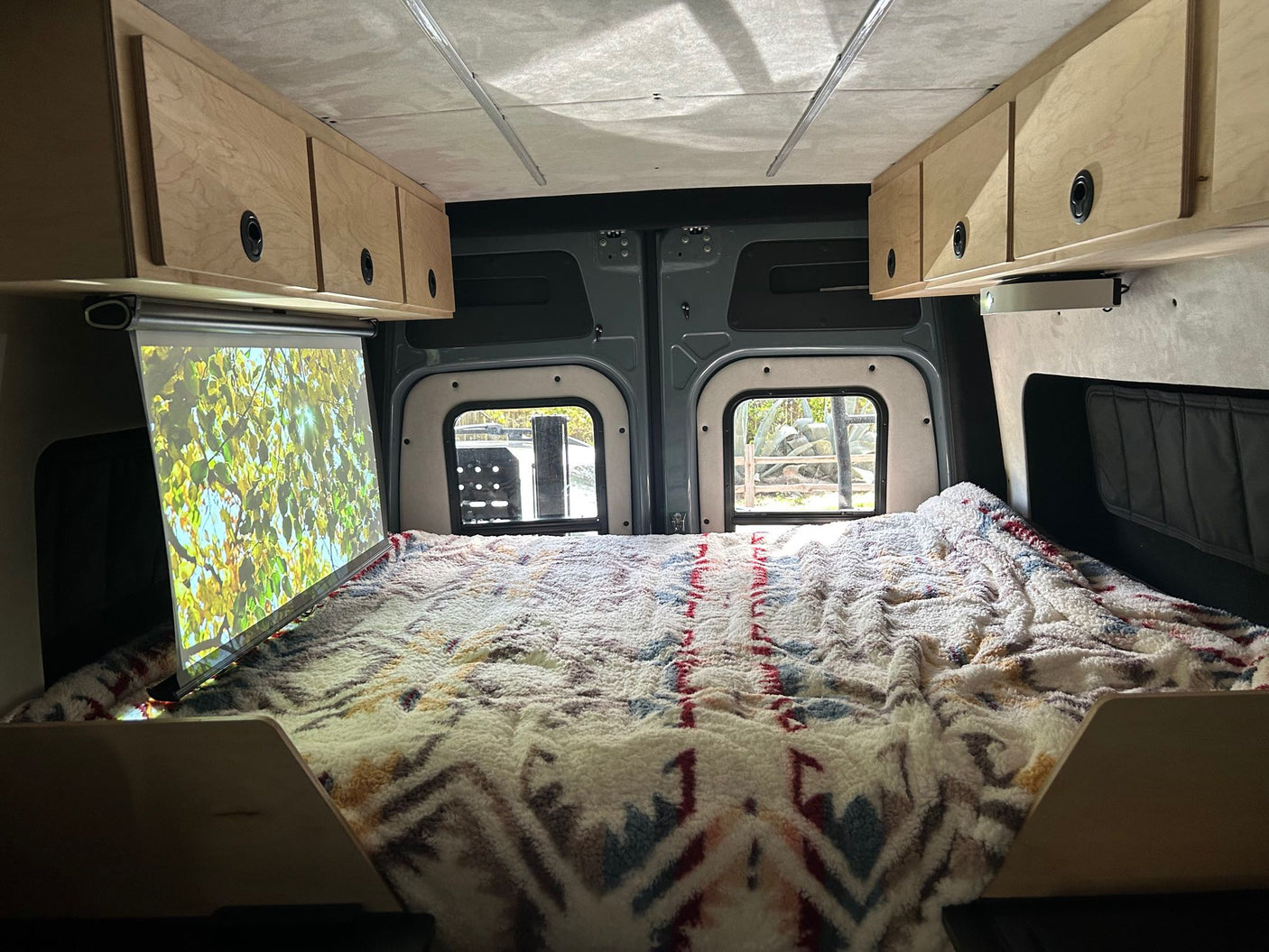 Cozy RV rental interior with a built-in projector screen over the comfortable bed and ample overhead storage.