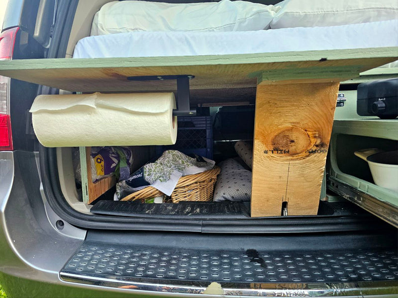 Optimized RV rental space: Back of a converted van/SUV with bed platform, paper towels, and storage for camping ease. — photo 9