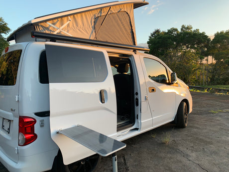 White pop-top camper van, with side door open and fold-out table, parked at sunset. Perfect RV rental for adventure.