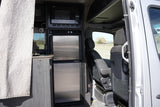 This RV rental interior displays a compact kitchen with microwave, two-door fridge, and the front cabin view through the open door.