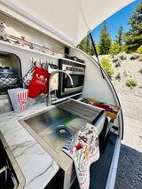 RV rental: compact outdoor kitchen with sink, microwave, "Life is Better at the Campsite" mitt, & nature views.