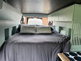 Cozy RV rental sleeping area features a large bed with gray waffle-knit bedding and sage green cabinets.
