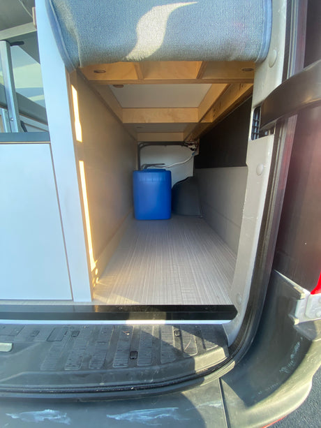 Spacious RV rental cargo area showing fresh and grey water tanks in a camper van's rear storage.