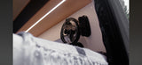 RV rental interior featuring a mounted fan, overhead strip lighting, and a bed with a white blanket in the foreground.