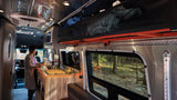Experience an RV rental: a cozy interior with a person making coffee, forest views, and smart storage.