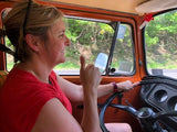 Happy woman gives thumbs up in an orange vintage campervan. Ready for an RV rental road trip adventure!