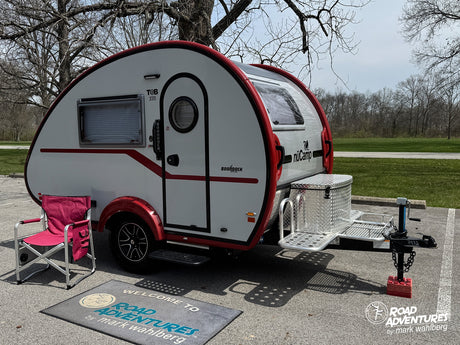This T@B 320 Boondock teardrop camper, an ideal rv rental for your next road trip adventure, is parked outdoors with a chair.