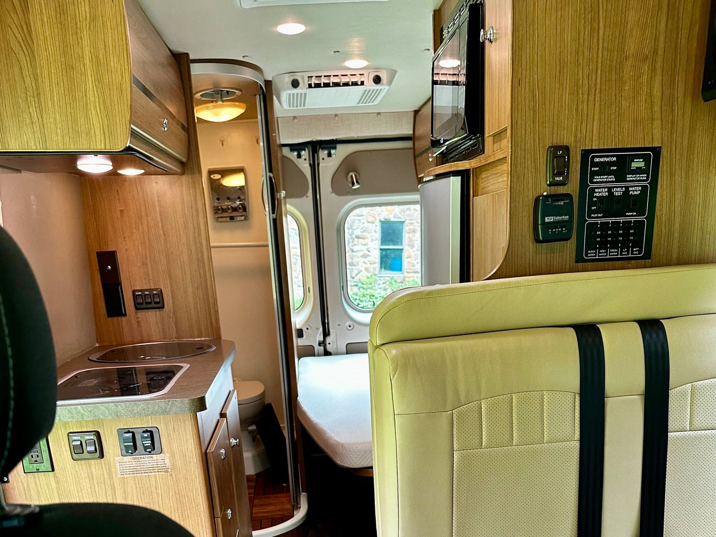  revealing interior seating & controls of the campervan.|Family enjoying a meal outside their RV rental van. Ideal for a camping trip or family road trip adventure.|RV rental kitchen featuring a compact Dometic two-burner stove and sink with hinged glass covers open.|Compact RV rental kitchen featuring a Dometic stovetop and sink — photo 13
