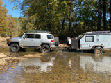 Adventure awaits! Silver SUV & Mission Overland RV rental traverse a rocky creek for off-road camping.