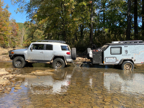 Adventure awaits! Silver SUV & Mission Overland RV rental traverse a rocky creek for off-road camping.