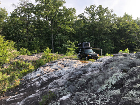 Land Rover with rooftop tent and awning on rocky terrain, ready for overlanding. An ideal RV rental for off-grid adventures!