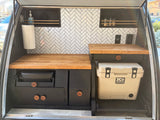 A compact, stylish RV rental kitchen featuring wood countertops, herringbone tiles, and built-in cooking gear and cooler.