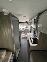 RV rental interior: compact kitchen with sink/stovetop, shower, and adaptable living space, viewed from rear.