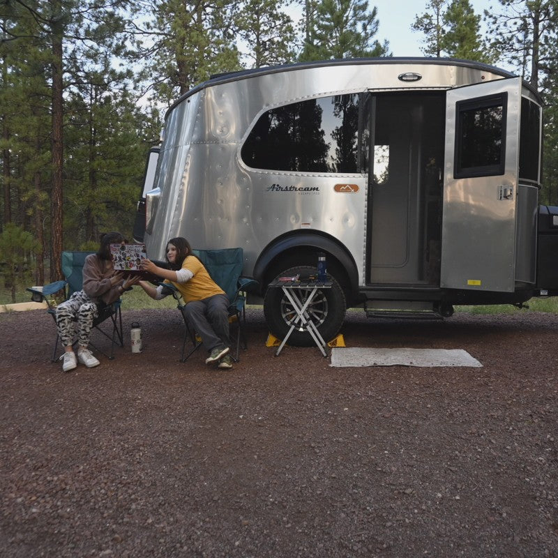 Friends relax, sharing a book by their Airstream RV rental at a peaceful campsite among pine trees. — photo 17
